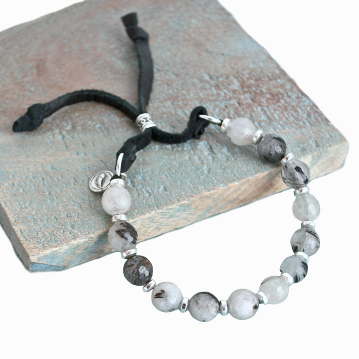 Stone Bracelet on genuine leather with a slide bead. Sterling silver accents and black rutilated quartz. Shown on a wood tile and a white background. 