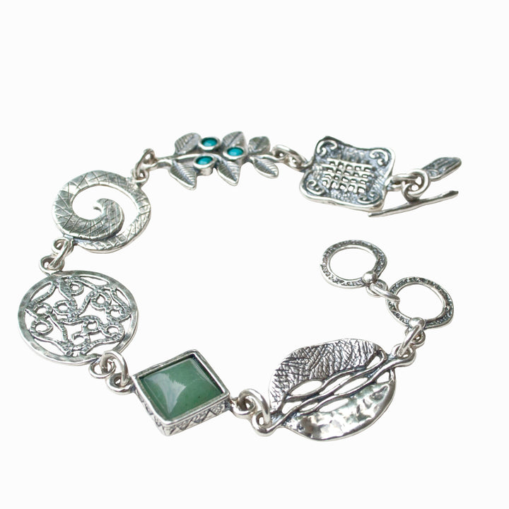 A sterling silver charm bracelet with a variety of linked chains and charms, including a turquoise stone and a green adventurine, with an adjustable toggle closure. Shown on a white background.