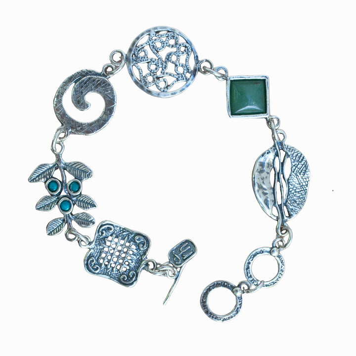 A sterling silver charm bracelet with a variety of linked chains and charms, including a turquoise stone and a green adventurine, with an adjustable toggle closure. Shown from above on a white background.