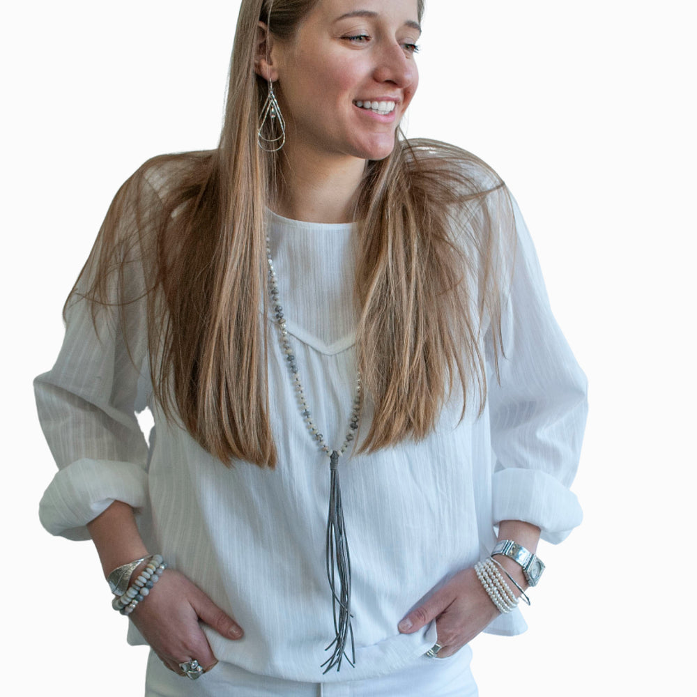 A handcrafted necklace with matte stone rondelle beads, silver-plated lava beads, and a grey faux leather tassel, knotted on a grey cord. Shown on a model.