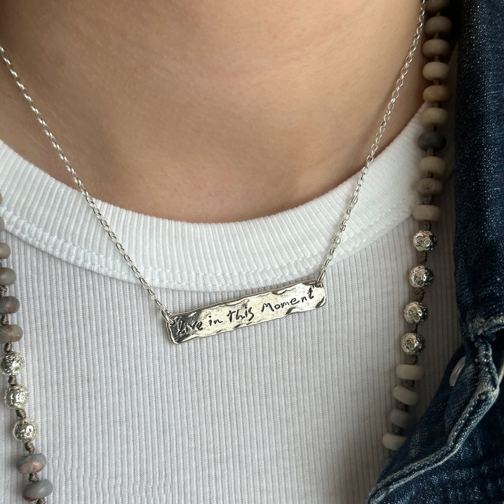 Sterling silver bar necklace wax cast with the words live in this moment. Shown on a model.