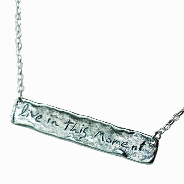 A sterling silver bar necklace with the words live in this moment. Close-up shot shown on a white background. 
