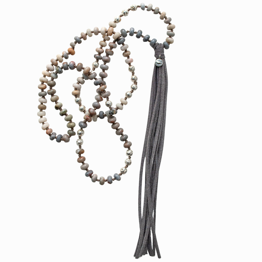 A handcrafted necklace with matte stone rondelle beads, silver-plated lava beads, and a grey faux leather tassel, knotted on a grey cord. Shown on a white background.