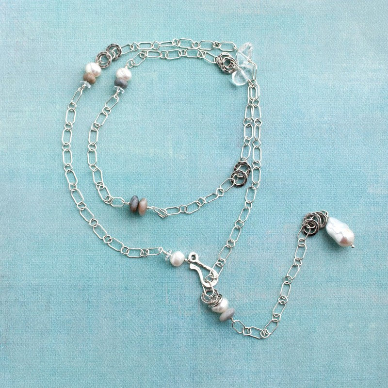A necklace with sterling silver, freshwater pearls, clear quartz, natural stone, and a beautiful focal baroque pearl. Shown on a blue background. 