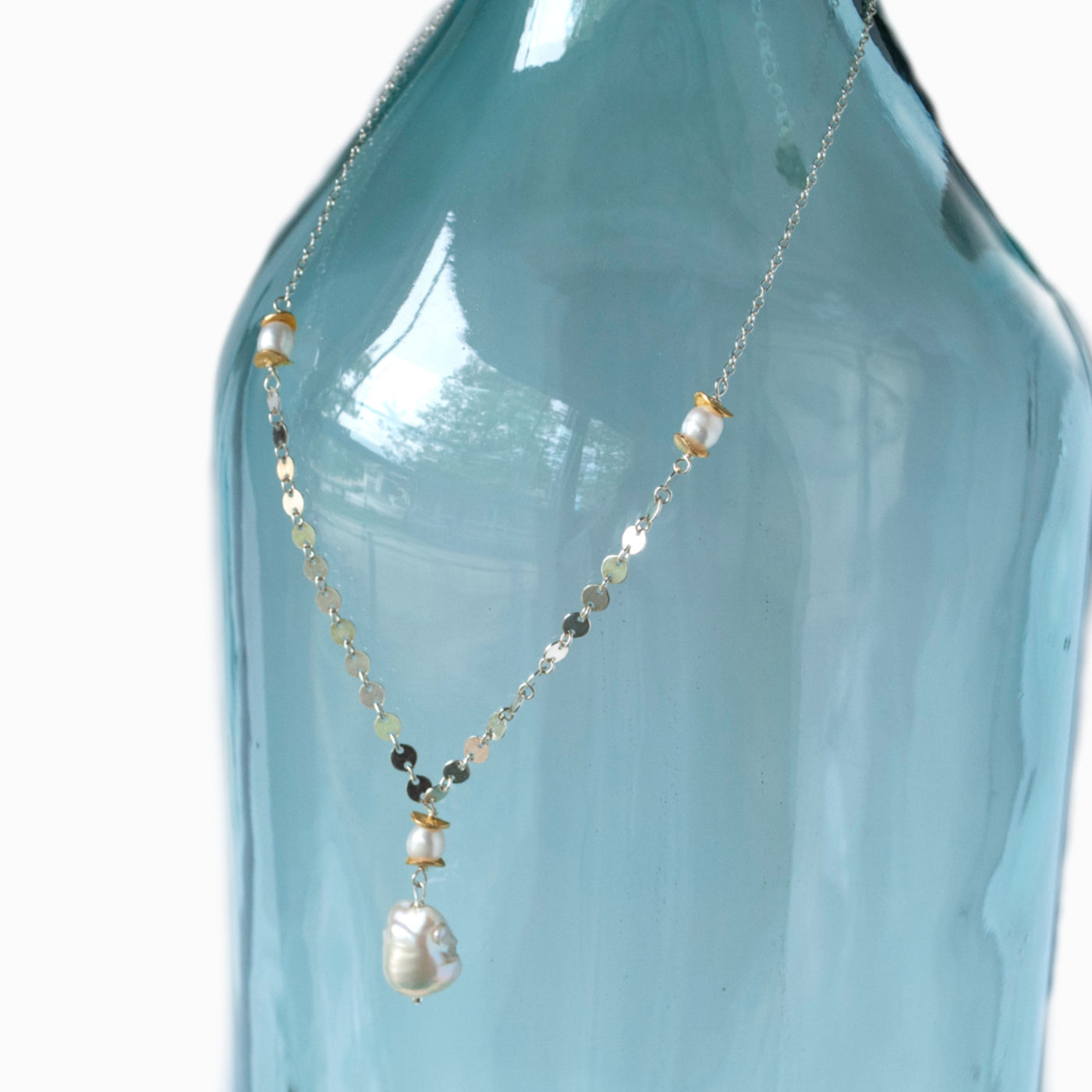 Baroque pearl necklace with sterling silver sequin chain, 22k gold plated accent beads. Shown on a aqua blue bottle.