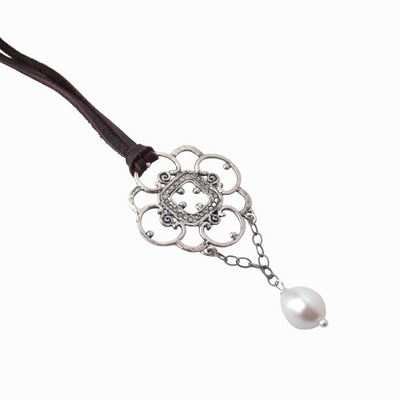 Close up photo of sterling silver lace pendant with a freshwater pearl dangle. The necklace is finished on chocolate brown leather lace.
