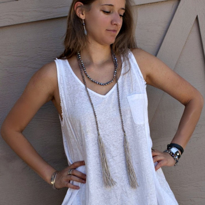 A lariat necklace with peacock freshwater pearls, grey agate, and grey cord, featuring long variegated tassels, is shown as a single necklace and open ends dangling on a model.