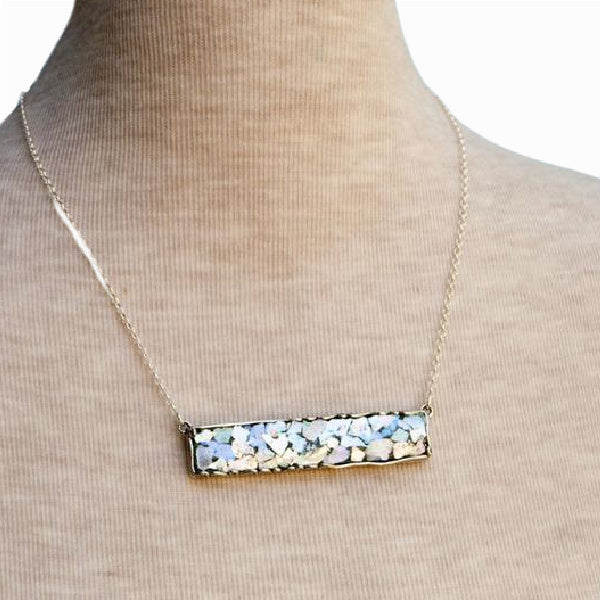 A sterling silver necklace with a bar pendant made of Roman glass is displayed on a mannequin.