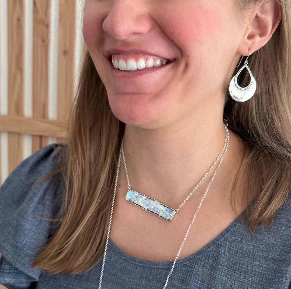 A sterling silver necklace with a bar pendant made of Roman glass is shown on a model. 
