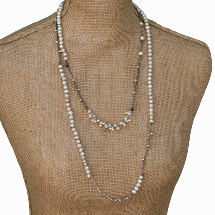 An asymmetrical necklace displayed on a mannequin, featuring freshwater pearls, sterling silver beads, a sterling sequin chain, and a braided silk blend cord. 