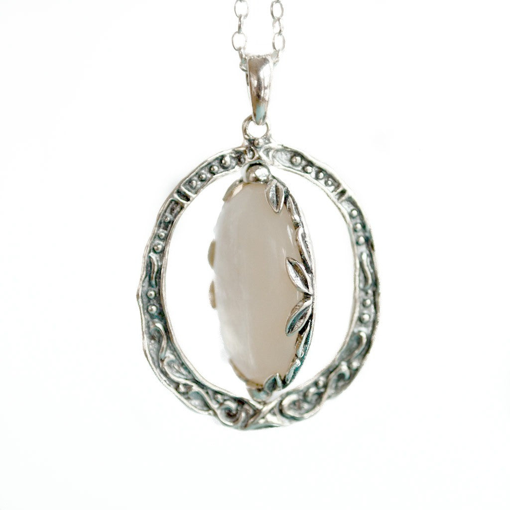 A sterling silver reversible necklace pendant with a filigree cross and mother-of-pearl on one side, and a plain mother-of-pearl on the reversible side, attached to a silver chain. A close-up shown on a white background. 