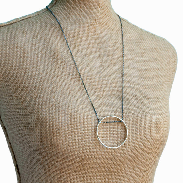Necklace with its oxidized sterling silver chain holds an organic circle of sterling silver. Shown on a mannequin. 