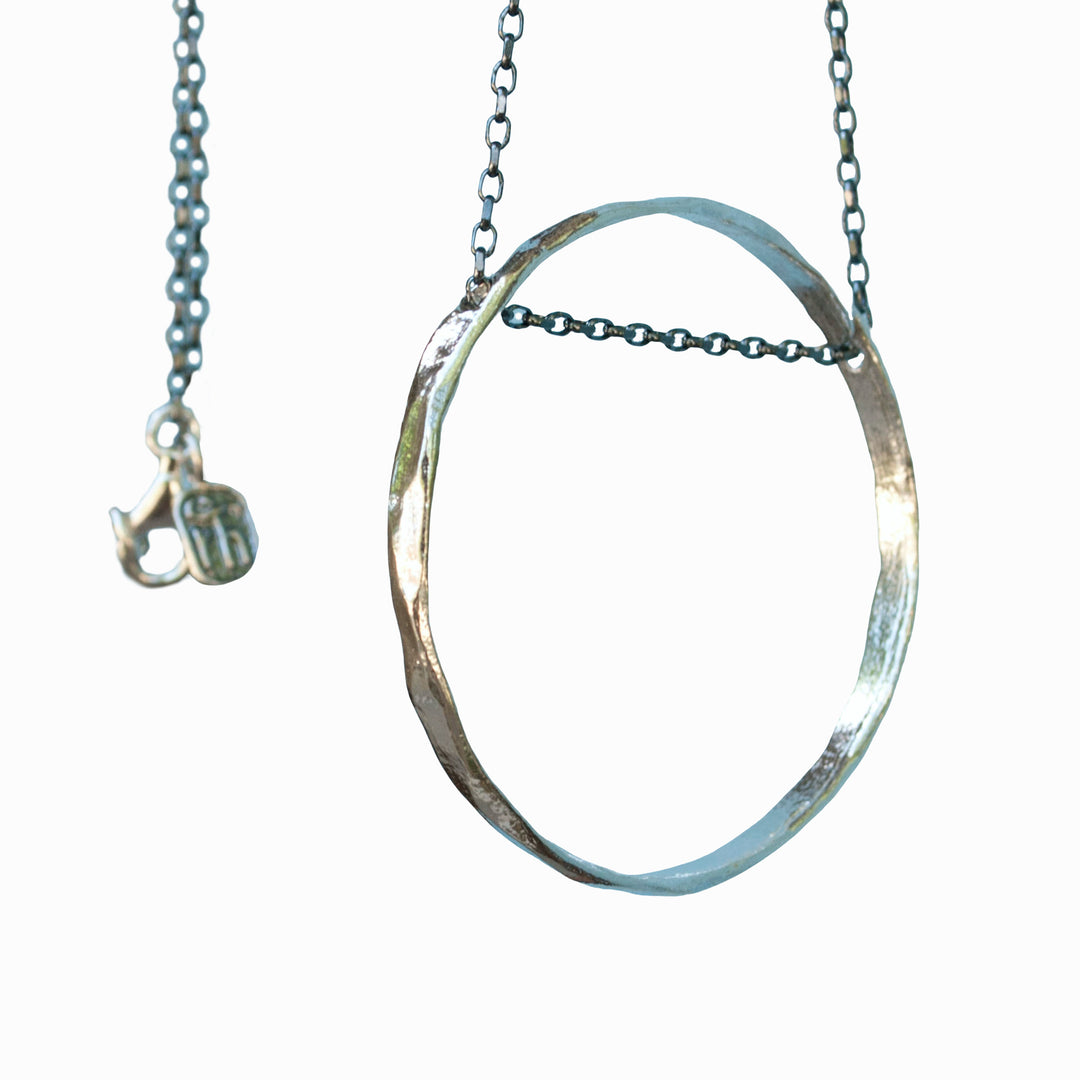 Necklace with an oxidized sterling silver chain holds an organic circle of sterling silver. Shown close-up on a white background. 