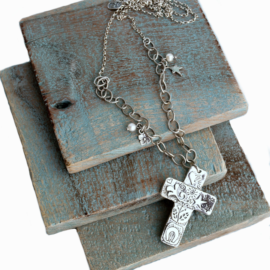 A sterling silver cross necklace with accent pearls, displayed on wooden tiles. A close-up view showing its beautiful details. 