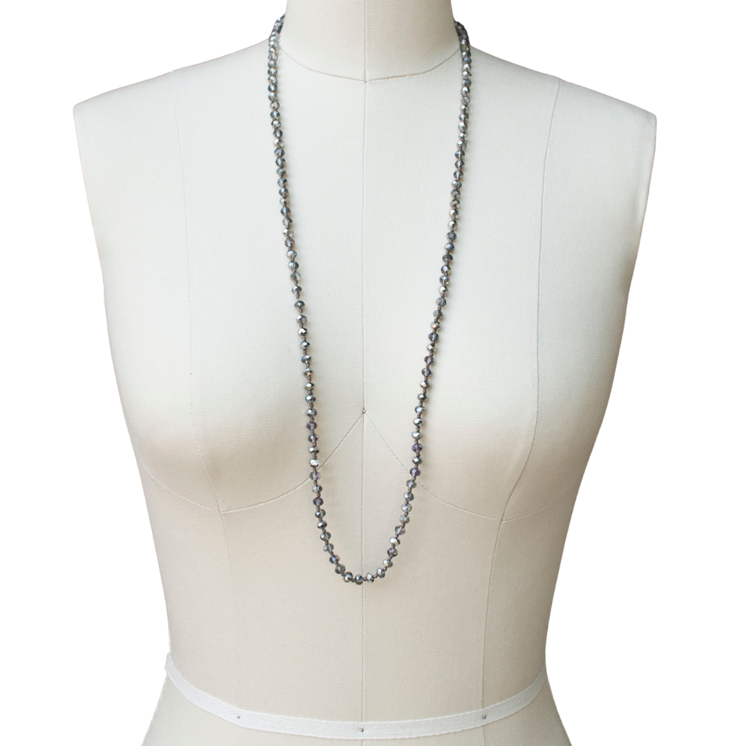 A single-strand, hand-knotted necklace made of faceted aurora borealis crystals is shown worn long on a mannequin. 