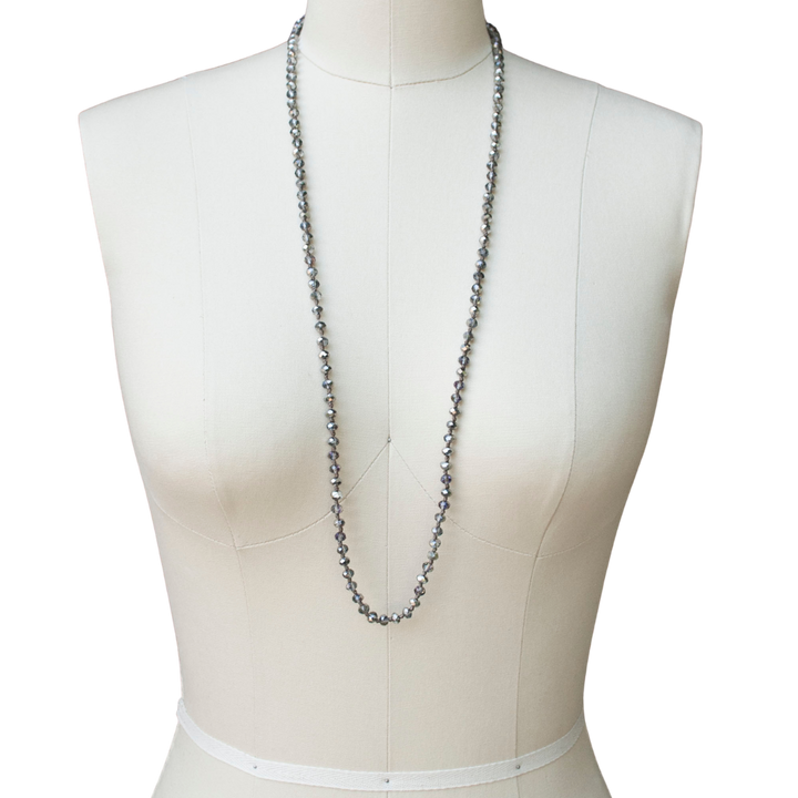 A single-strand, hand-knotted necklace made of faceted aurora borealis crystals is shown worn long on a mannequin. 