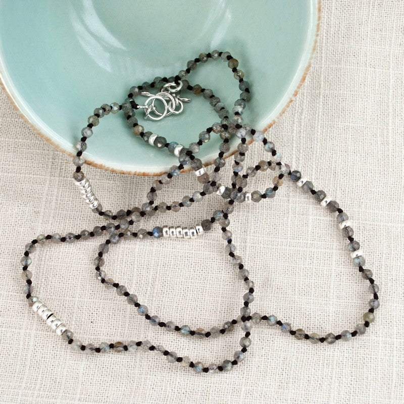 A labradorite necklace with sterling silver accents, displayed draped over a a small blue dish. Shows its adjustable toggle closure as well. 