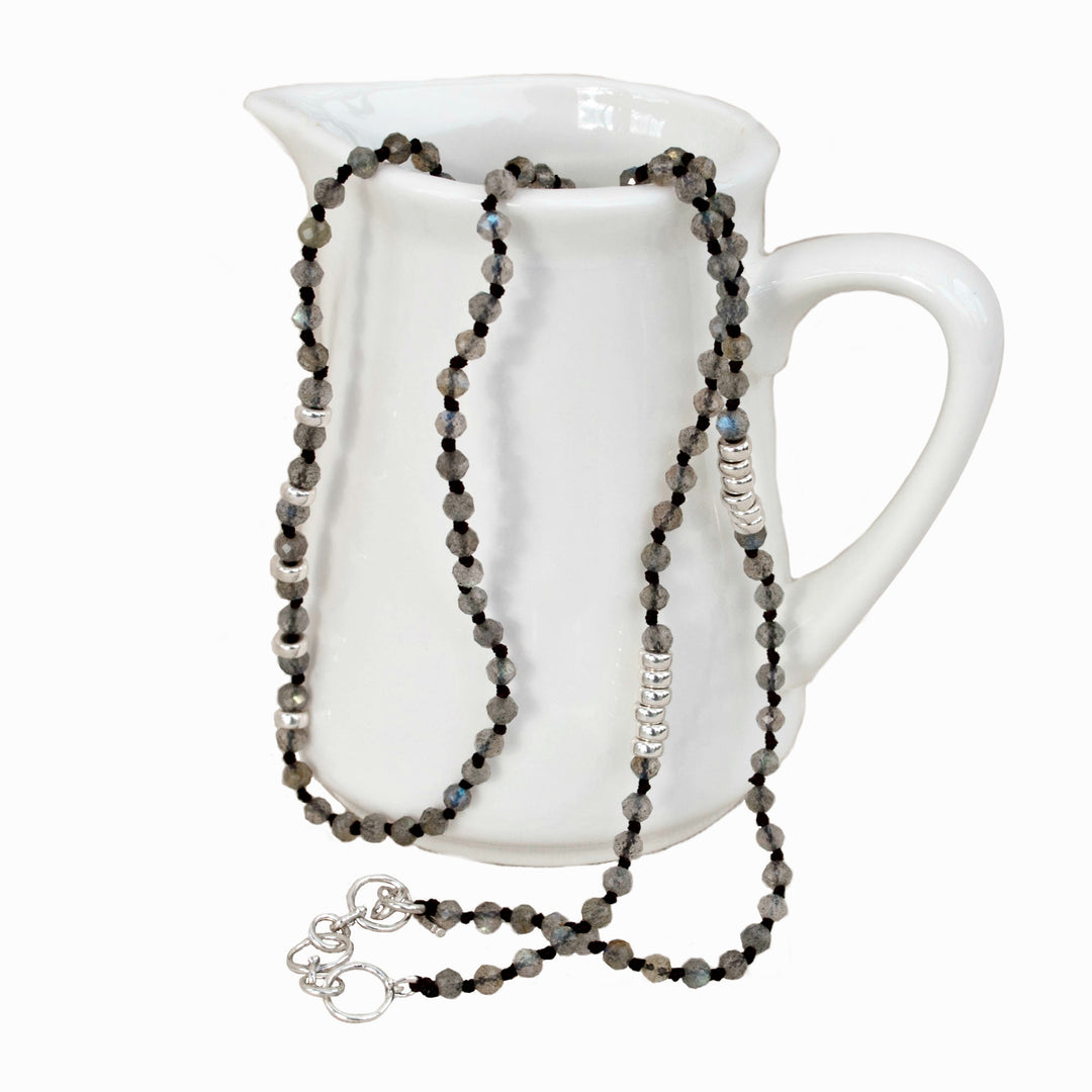 A labradorite necklace with sterling silver accents, displayed draped over a white ceramic pitcher. Shows its adjustable toggle closure as well. 