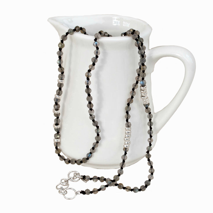 A labradorite necklace with sterling silver accents, displayed draped over a white ceramic pitcher. Shows its adjustable toggle closure as well. 
