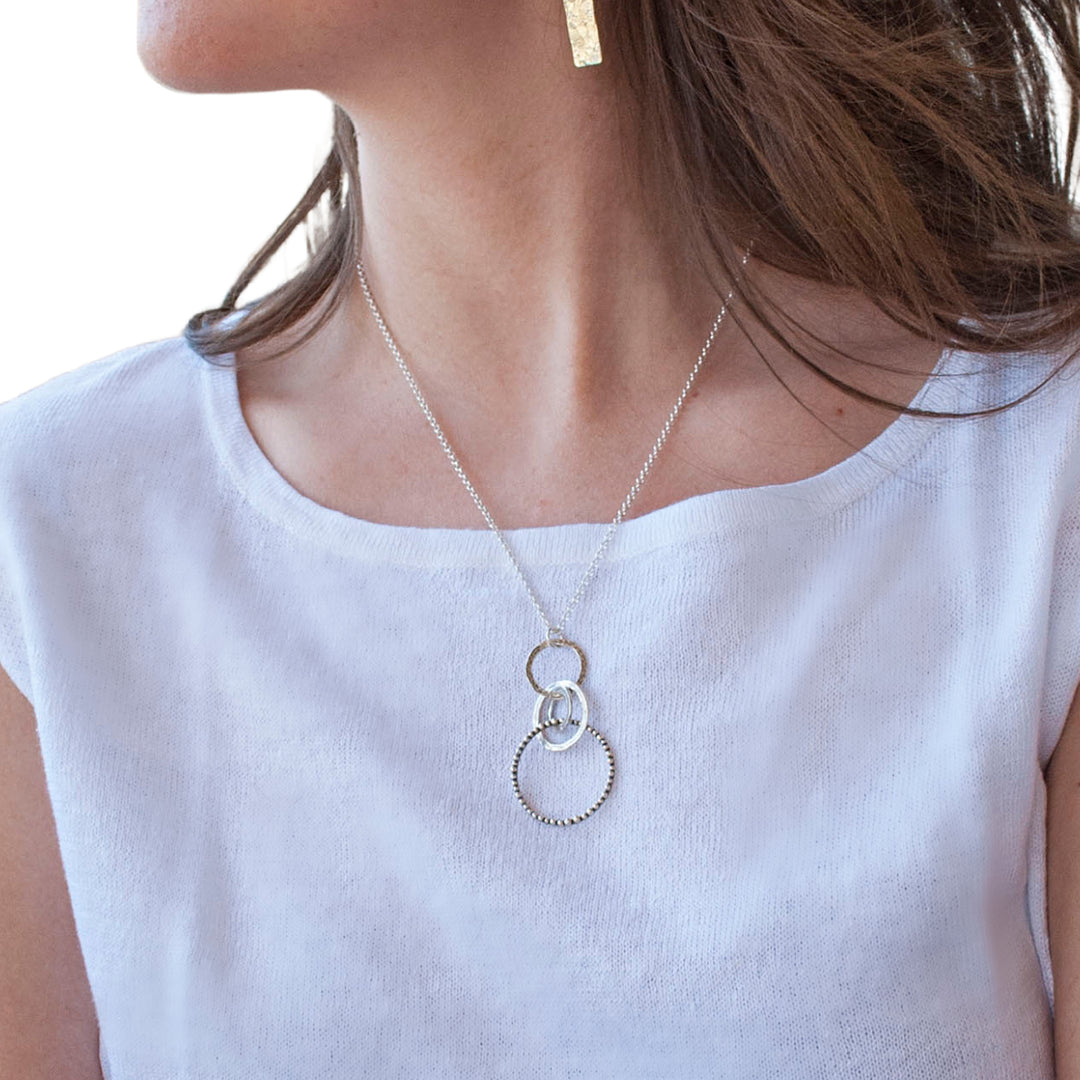 A sterling silver necklace with a chain link, featuring a series of interlocking circles in varying sizes and a round pendant with a design. Shown on a model.