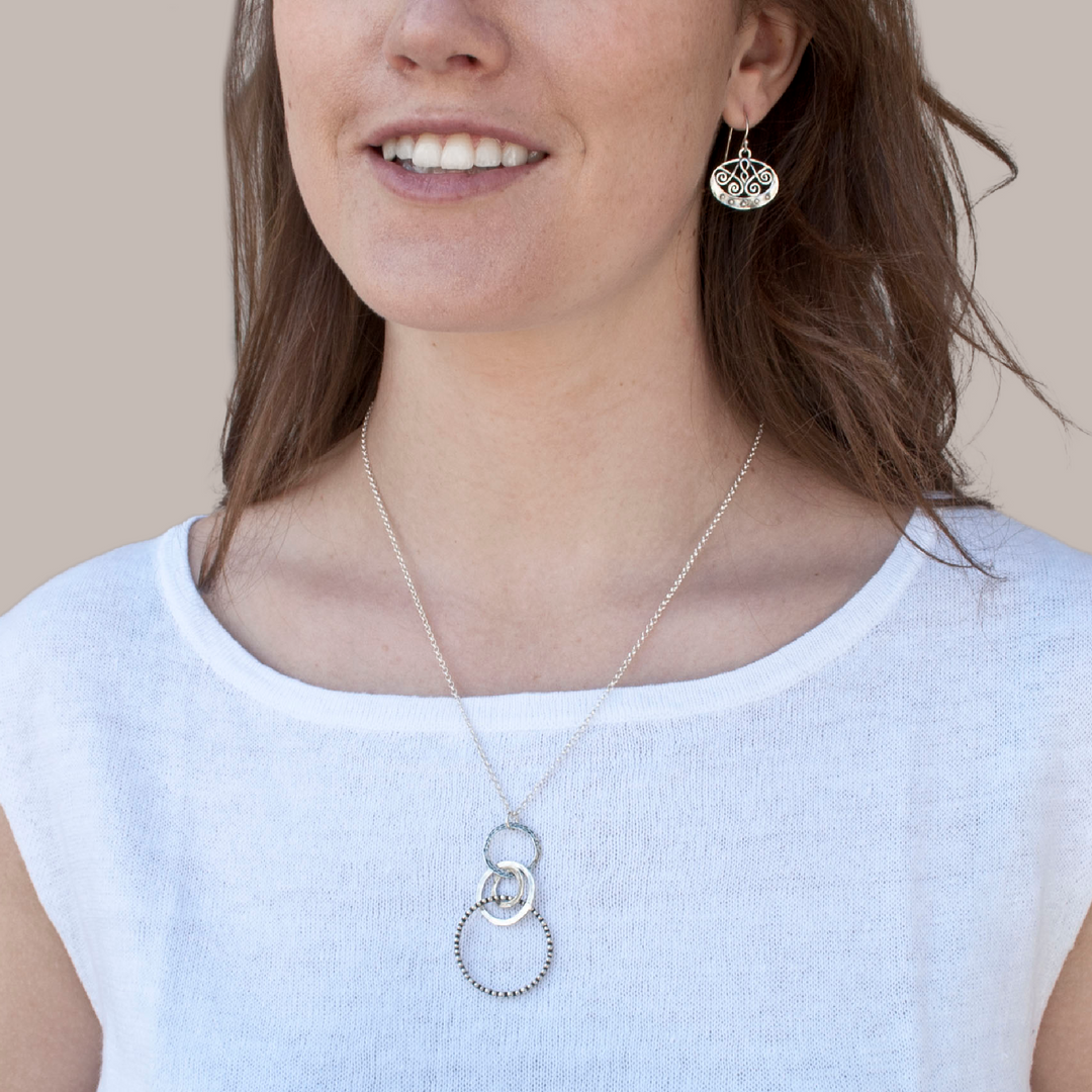A sterling silver necklace with a chain link, featuring a series of interlocking circles in varying sizes and a round pendant with a design. A close-up showing its dotted details and hammered texture on a model.