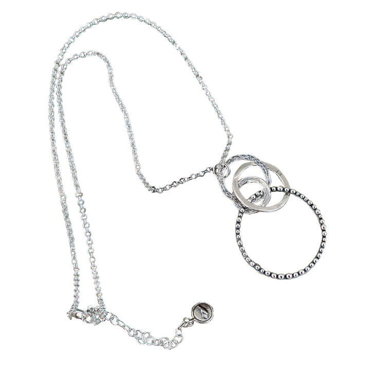 A sterling silver necklace with a chain link, featuring a series of interlocking circles in varying sizes and a round pendant with a design. Shown on a white background. 