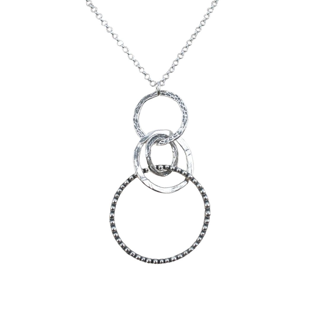 A sterling silver necklace with a chain link, featuring a series of interlocking circles in varying sizes and a round pendant with a design. A close-up showing its dotted details and hammered texture on a white background. 