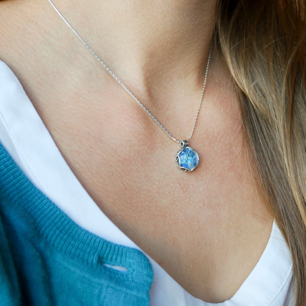 A Roman glass necklace with a silver chain and a silver crown bezel setting is shown on a model. 