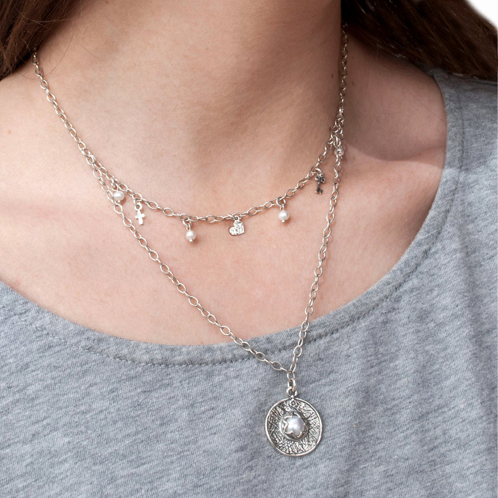 A layered pearl necklace with sterling silver chains and a central bezel-set pearl pendant, is shown on a model. 