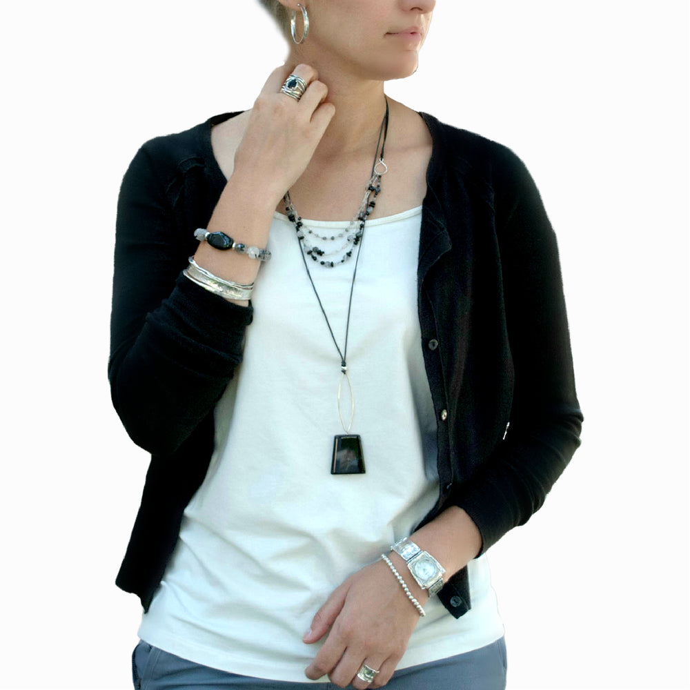 A multi-strand necklace with black agate and tourmalinated quartz beads, sterling silver chains, on a black leather is shown on a model layered with coordinatig jewelry.