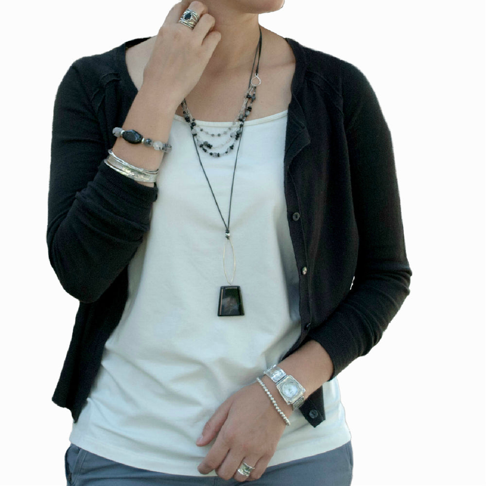 A trapeze necklace with a black agate pendant and sterling silver accents, is shown on a model. 