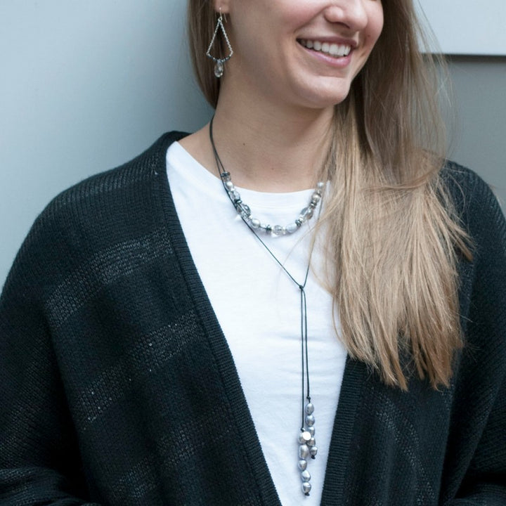 A lariat necklace with gray freshwater pearls, hematite, and crystal, shown on a model.
