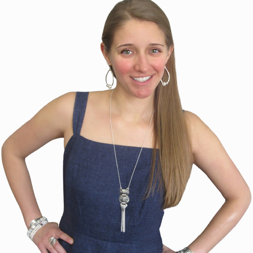 A silver pendant-style necklace with three linked textured silver pieces with a silver tassel is shown on a model. 