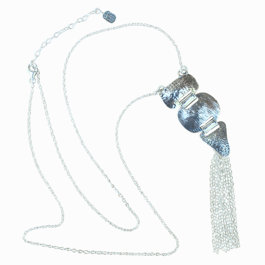 A silver pendant-style necklace with three linked textured silver pieces with a silver tassel, on a white background.