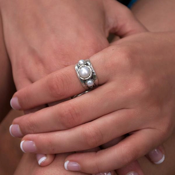 A sterling silver ring with a swirl detail band and three white freshwater pearls. One larger center pearl with a smaller pearl flanking each side. Shown on a model. 