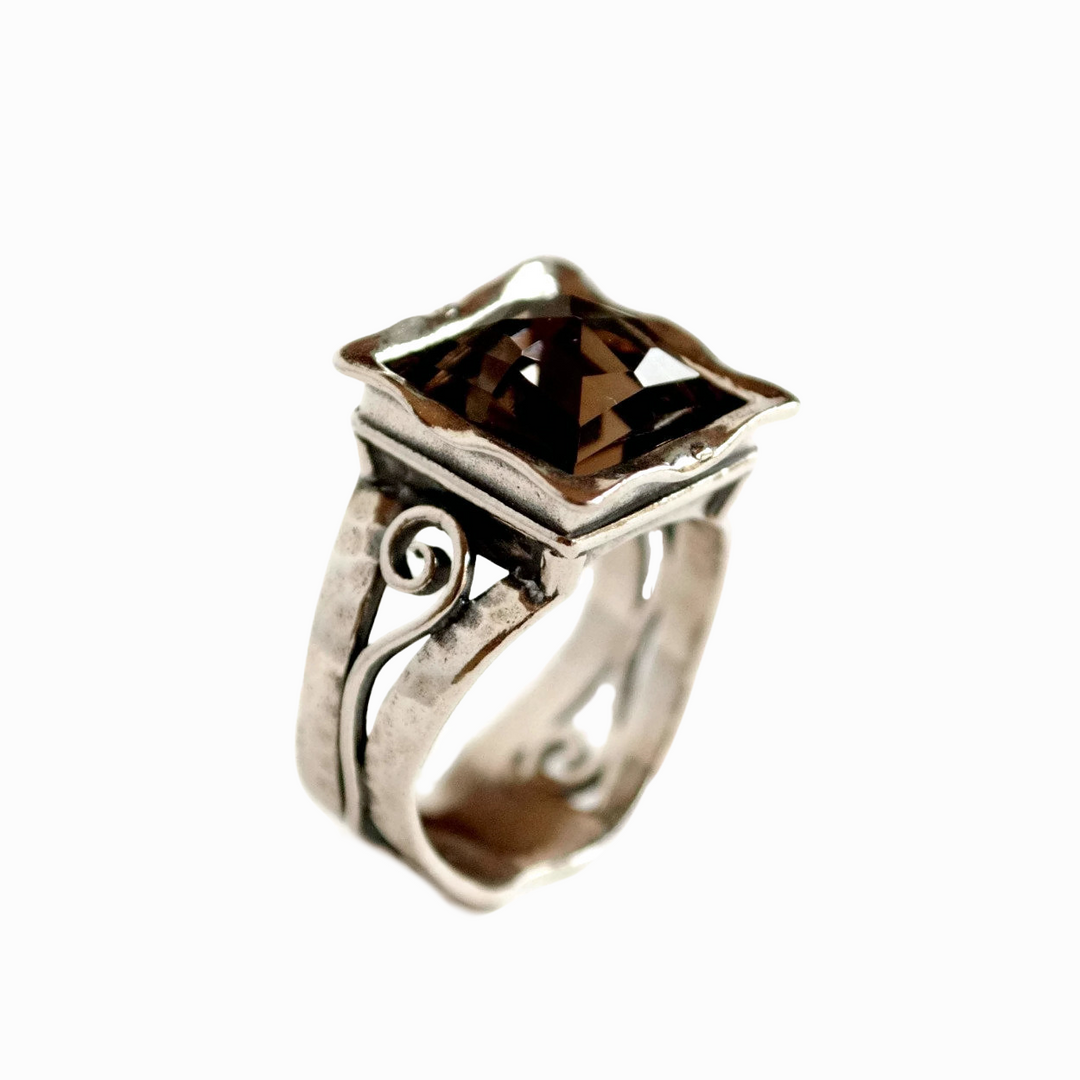 A sterling silver ring with a faceted smoky quartz centerpiece, featuring intricate details and a square shape. Side view shown on a white background.