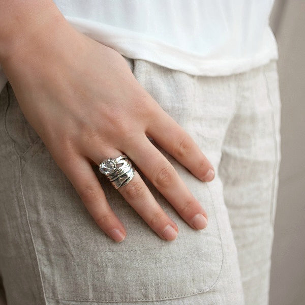 A sterling silver ring with a large, clear cubic zirconia and featuring a wide band design with a tapered back. Shown on a model.