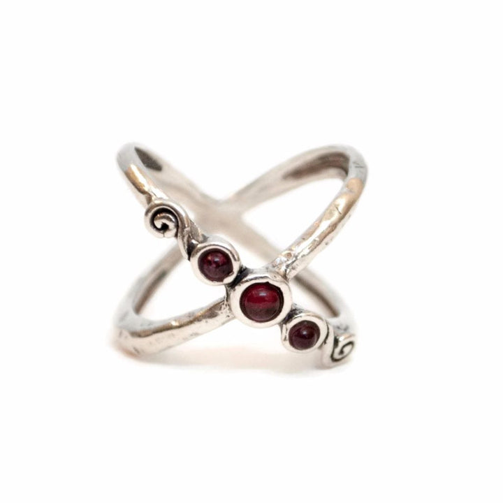A sterling silver criss-cross ring with three garnet stones at the intersection of the bands is shown on a white background.