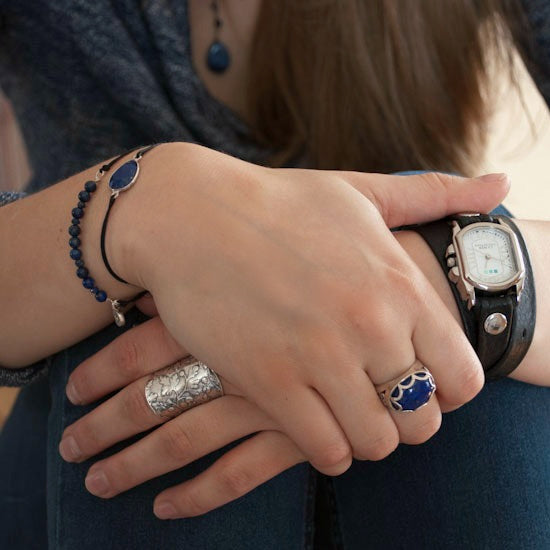 A sterling silver ring with a raised cross design on a curved band, featuring lined details. Shown on a model.