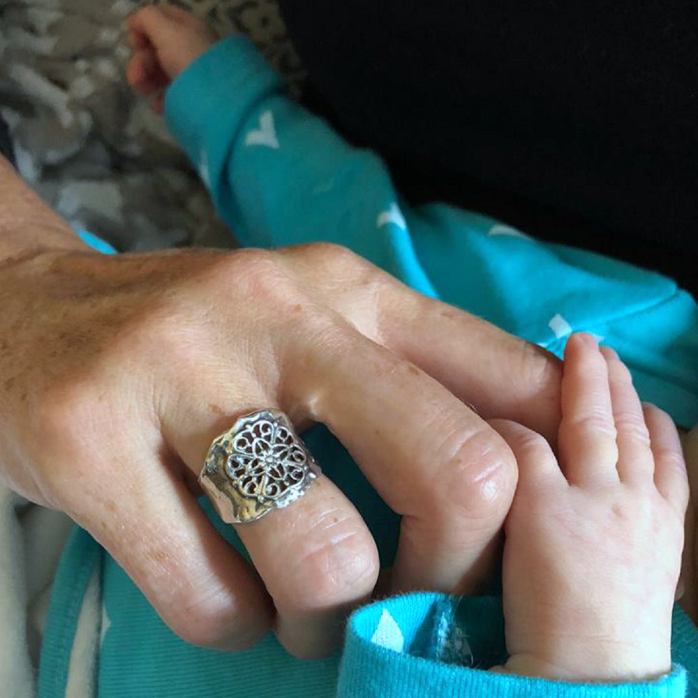 A sterling silver ring with floral lace-like details is shown on a model.