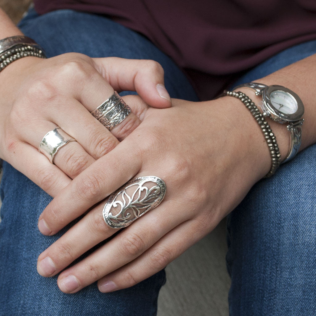 A sterling silver ring with intricate open scroll work, slightly oxidized for depth and detail, is shown on a model. 