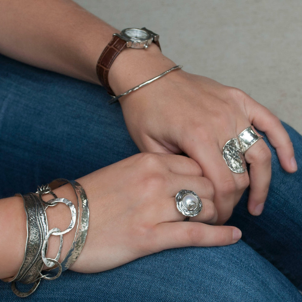 A ring with a freshwater pearl set in a sterling silver band with swirl details is shown on a model. 
