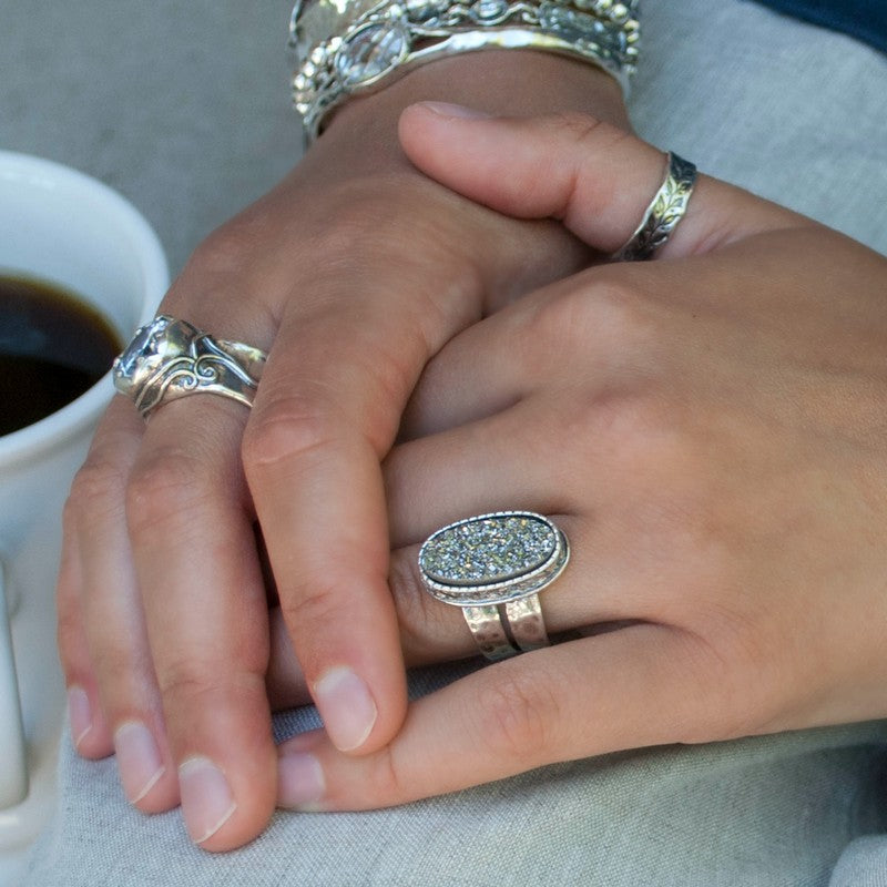 A sterling silver ring with a central oval-shaped druzy quartz stone, featuring a double-hammered band and a comfort fit design. It is shown on a model. 