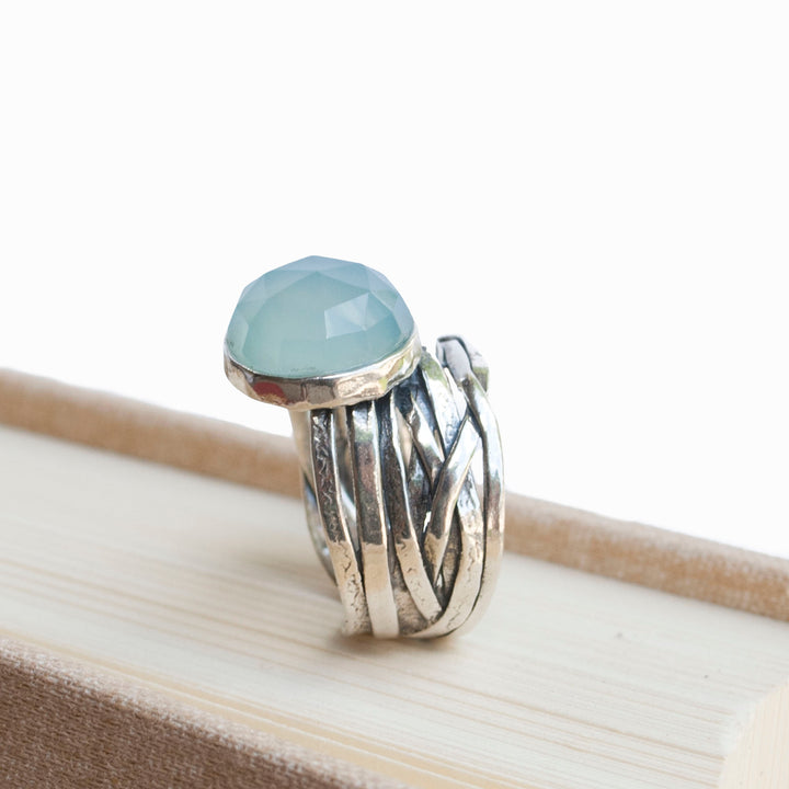 A sterling silver ring with a faceted aqua chalcedony dome on a chunky band, displayed on a book.