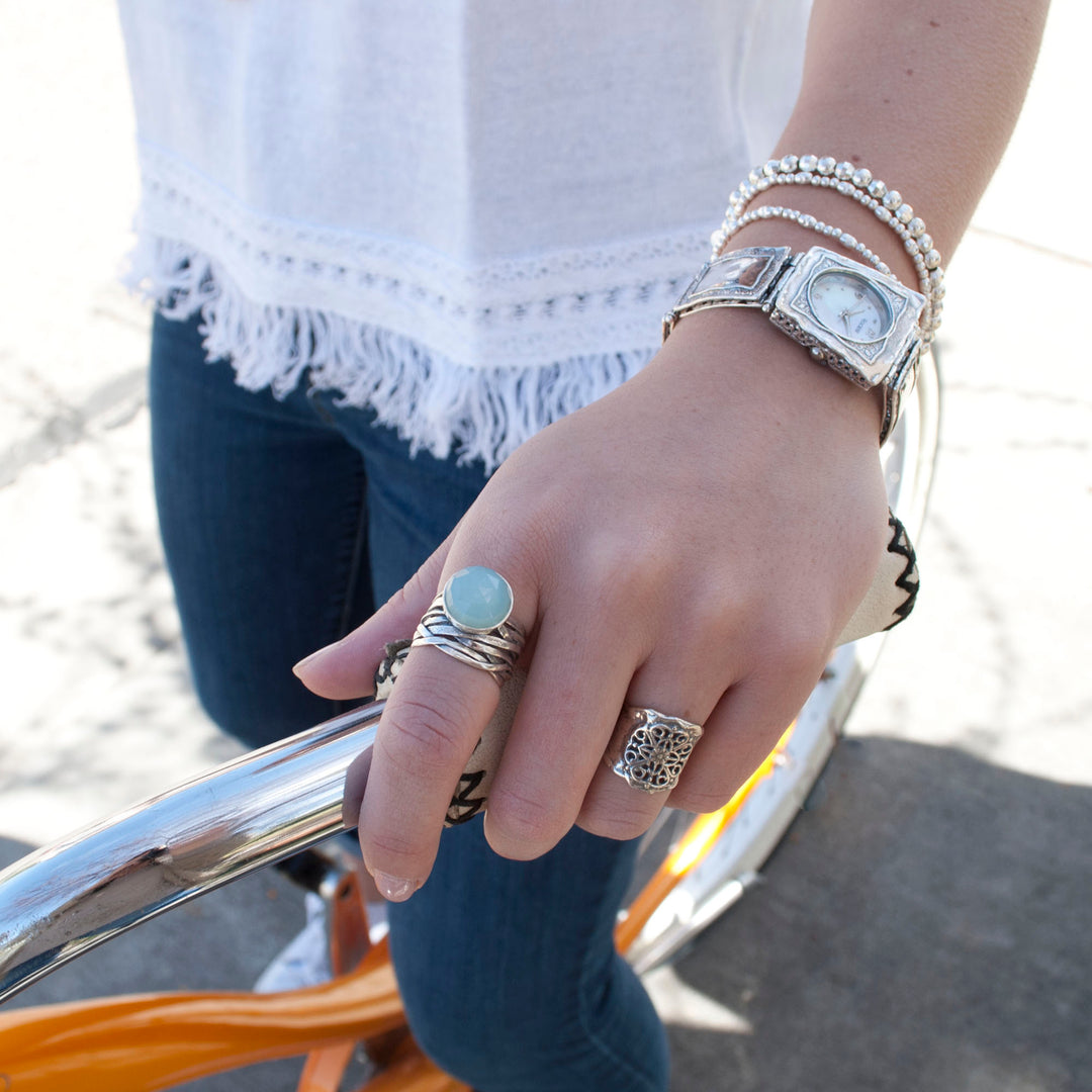 A sterling silver ring with a faceted aqua chalcedony dome on a chunky band, is shown on a model. 