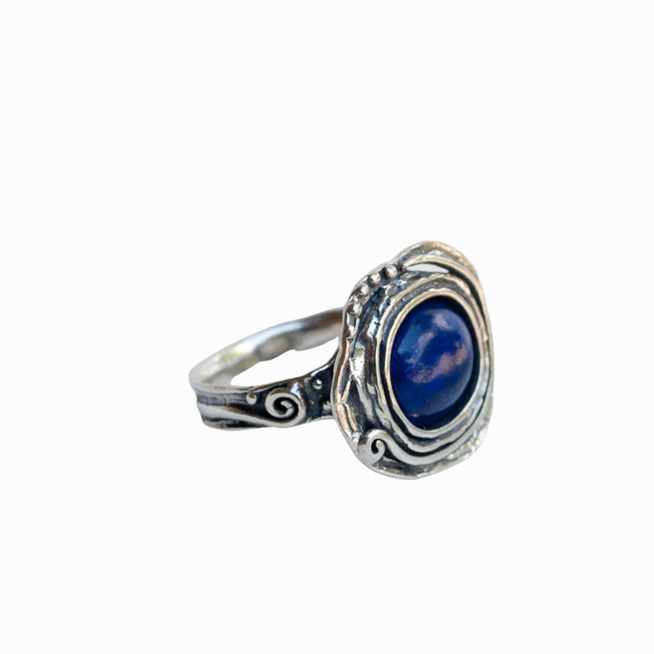 A sterling silver ring with a deep blue cabochon stone, designed with intricate patterns around the band. Is shown on a white background.