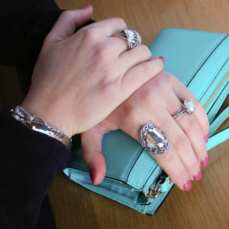 A sterling silver ring with a textured, organic border with a prominent, rounded hammered surface. Shown on a model. 