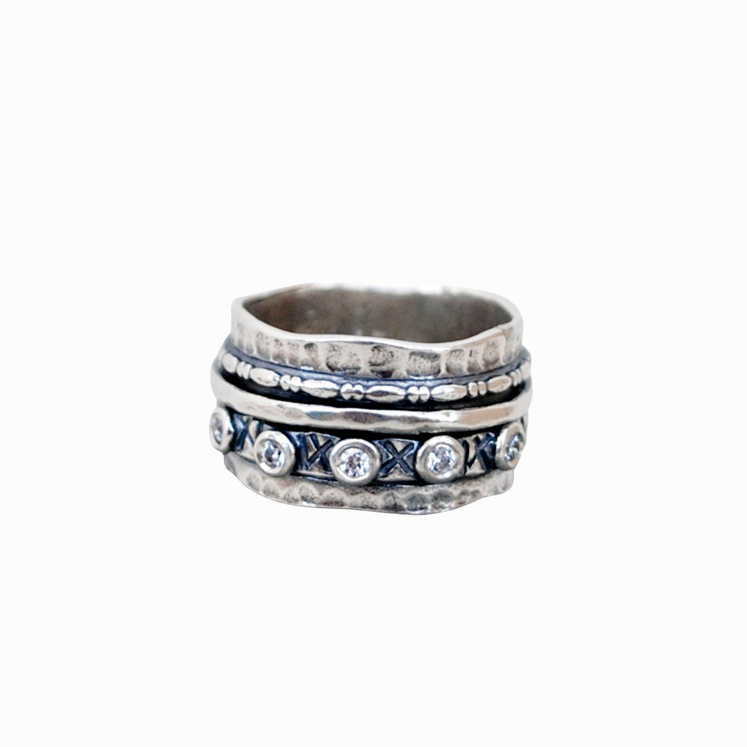 A sterling silver spinner ring with CZ stones and oxidized finish, featuring X and O motifs, is shown on a white background.