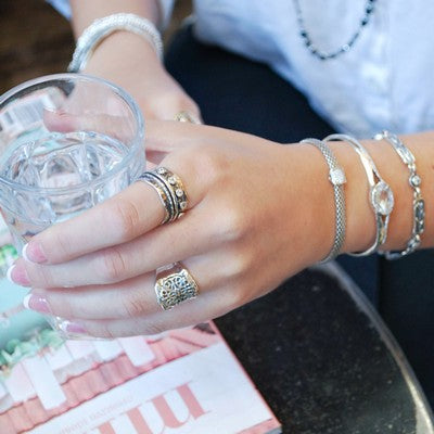 A sterling silver spinner ring with CZ stones and oxidized finish, featuring X and O motifs, is shown on a model. 