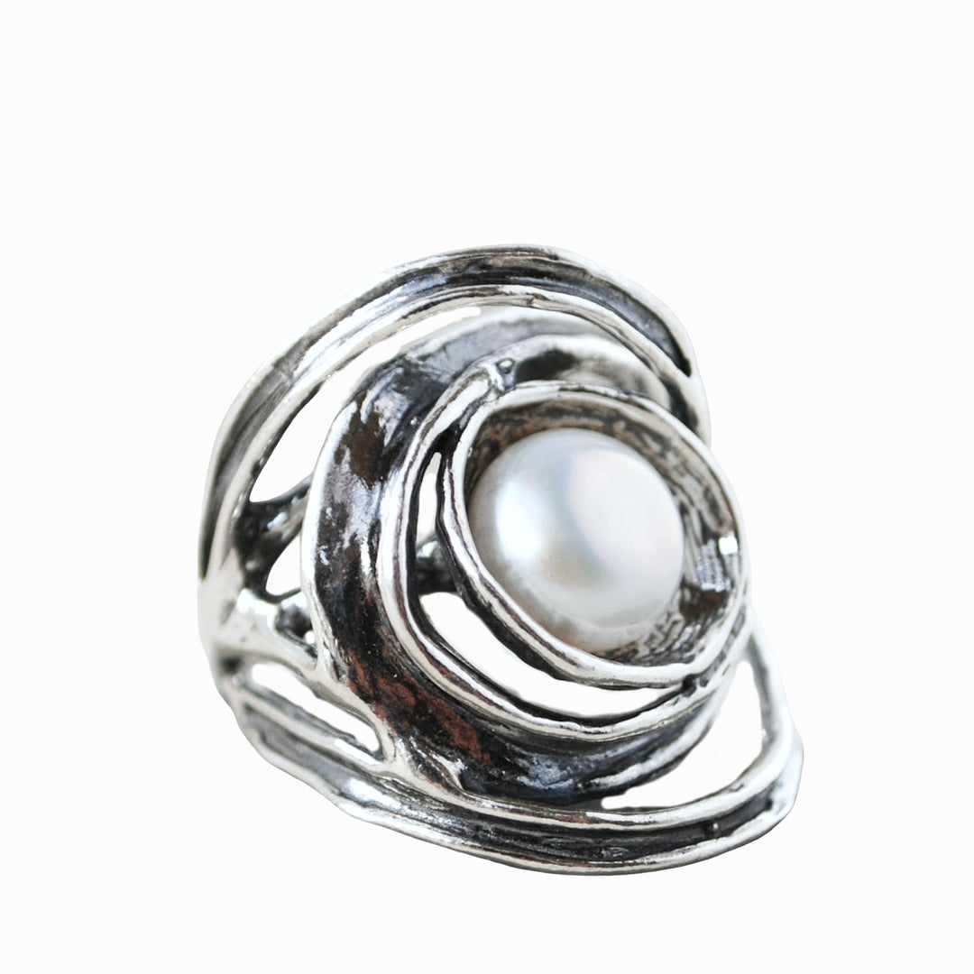 An artisan-crafted sterling silver ring with a freshwater pearl centered amidst swirling silver designs. Shown on a white background. 